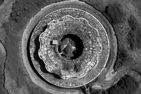 A black-and-white aerial photograph looking down on a circular mine-type structure set in the earth.
