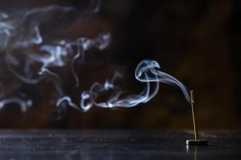 A photograph of smoke billowing from a lit incense stick.
