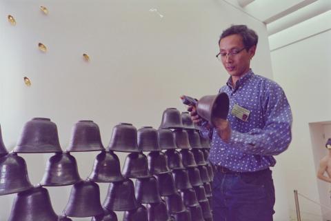 An artist installs a sculptural work made of bell shapes.