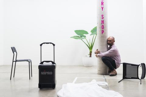 A performance artist crouches in a bright gallery space, hugging a pole
