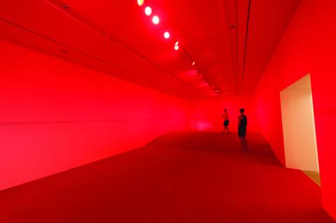 An installation of a long gallery space entirely painted and/or lit in bright red, with two Gallery visitors at the space's far end.