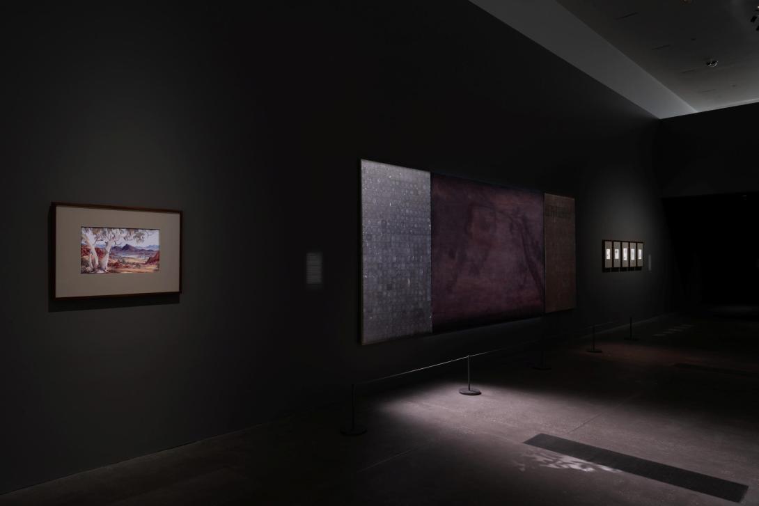An installation view of a dark gallery space with work hung on the walls.